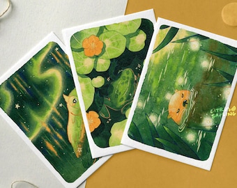 May include: Three watercolor illustrations on white cardstock. The first shows a green owl with a starry night sky background. The second shows a green frog in a pond with lily pads and yellow flowers. The third shows a yellow otter swimming in a pond with fireflies.