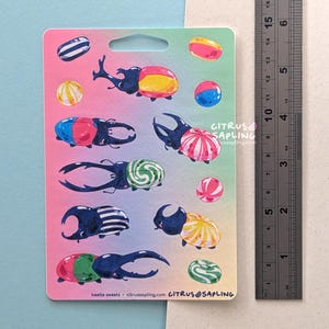 May include: A sticker sheet featuring colorful illustrations of beetles with candy-like designs. The beetles are in various colors, including blue, red, yellow, and green. The text "beetle sweets - citrussapling.com" is visible.