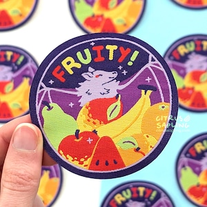 May include: A circular embroidered patch with a dark purple border featuring a light purple bat with outstretched wings above a colorful arrangement of a green pear, a red apple, a slice of watermelon, and yellow bananas with the text FRUITY!