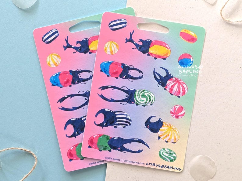 May include: Two sticker sheets with colorful illustrations of beetles and candies. The beetles are depicted with various patterns and colors, and the candies are round and striped. The background is a gradient of pink and green.
