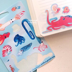 May include: A sheet of sea creature stickers and a notebook. The stickers feature colorful illustrations of an octopus, squid, nautilus, and other marine life. The notebook has a pink octopus sticker on the corner. The brand name "CITRUS@SAPLING" is visible.