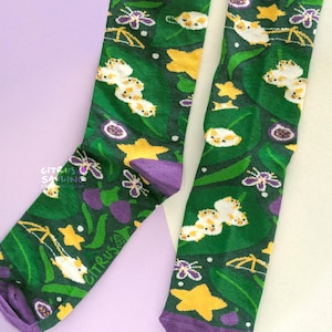 May include: A pair of green socks with a repeating pattern of white, yellow, and purple floral and insect designs. The socks have purple toes and cuffs. The text "CITRUS SALINE" is printed on the side of one sock.