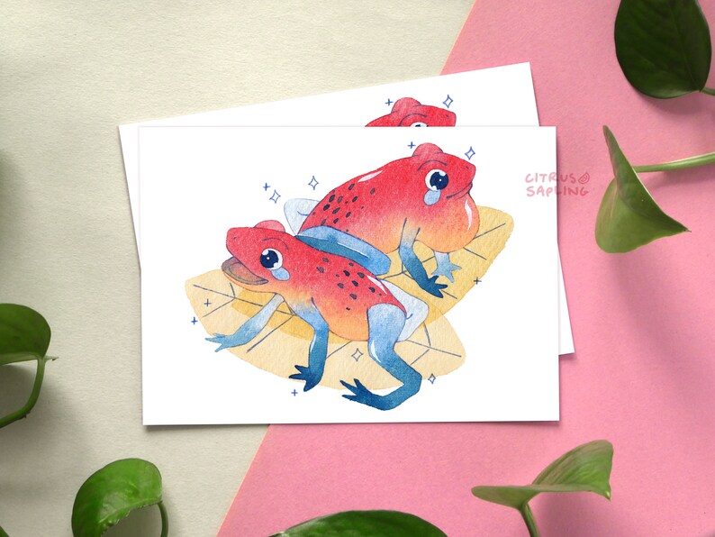 May include: Two red and orange poison dart frogs with blue accents are sitting on yellow leaves with white sparkles. The frogs are facing each other and have a sad expression. The text "CITRUS SAPLING" is in the top right corner of the image.