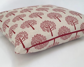 May include: Square decorative pillow with a repeating pattern of red trees on a beige background. The pillow has a red zipper and trim, and is likely made of a linen or cotton blend fabric. The design is suitable for home decor.