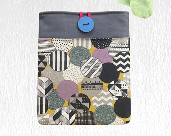 May include: A fabric tablet sleeve with a gray top and a patterned bottom. The bottom features a yellow background with various sized circles in black, white, gray, and purple. A blue button secures the top flap.