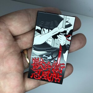 May include: Black and white enamel pin featuring a character with a sword and a red background. The text "戦国時代" is written in red on the bottom of the pin.