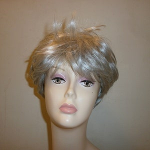 May include: A short, silver-grey wig with a side parting and a slightly messy style.