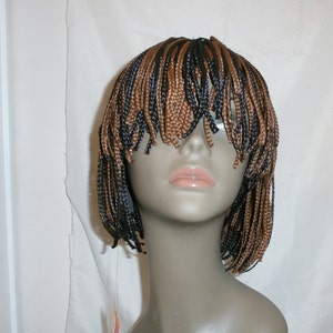 May include: A brown and black braided wig with a short bob style. The wig is on a mannequin head.