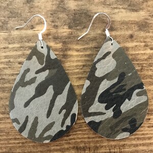May include: A pair of teardrop-shaped earrings with a camouflage pattern in shades of green, brown, and gray. The earrings have silver hooks.