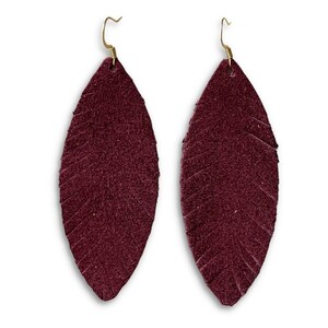 May include: A pair of burgundy leather earrings shaped like feathers. The earrings have a simple gold hook closure.