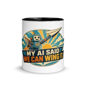 May include: A white ceramic mug with a black rim featuring a graphic of a blue robot holding a paper airplane. The design includes a yellow sunburst background with clouds and the text MY AI SAID WE CAN WING IT in bold blue and orange lettering.