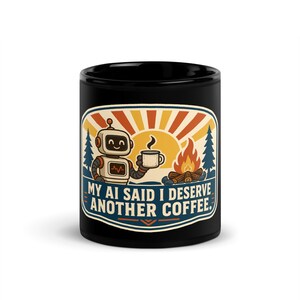 Puede incluir: Una taza de cerámica negra con el gráfico de un robot sonriente sosteniendo una taza de café junto a una fogata. El fondo muestra un sol y pinos. El texto dice: "MY AI SAID I DESERVE ANOTHER COFFEE." El diseño utiliza colores naranja, azul y crema.