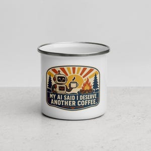 Puede incluir: Una taza de esmalte blanco con borde plateado que presenta un gráfico de un robot sosteniendo una taza de café junto a una fogata bajo un sol. El texto dice MY AI SAID I DESERVE ANOTHER COFFEE. El diseño incluye pinos y colores naranja, azul y amarillo.