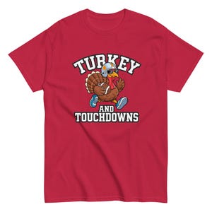 Könnte beinhalten: Rotes T-Shirt mit einer Cartoon-Truthahn-Illustration, die einen Footballhelm und eine Sonnenbrille trägt und einen Football hält. Der Text "TURKEY AND TOUCHDOWNS" ist aufgedruckt.