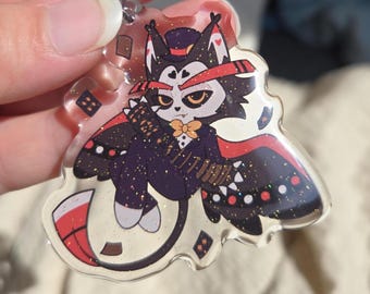 Puede incluir: Un llavero de acrílico transparente con una ilustración estilizada de un personaje felino que lleva un sombrero de copa, una pajarita y un traje oscuro con detalles rojos. El personaje está rodeado de pequeños símbolos de cartas de juego y tiene brillo.