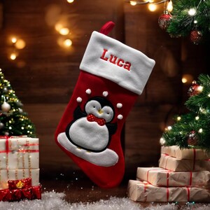 Può includere: Calza di Natale rossa e bianca con un design di pinguino e il nome "Luca" ricamato sul polsino.