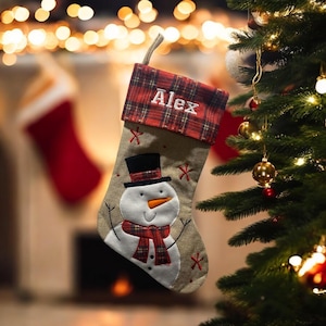 May include: A beige Christmas stocking with a snowman applique and a red tartan cuff. The stocking is personalised with the name "Alex".