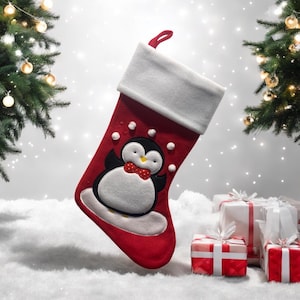 Peut inclure: Chaussette de Noël rouge avec un revers blanc et un motif de pingouin. Le pingouin porte un nœud papillon et a du duvet blanc. La chaussette est posée sur une surface blanche avec des cadeaux emballés.