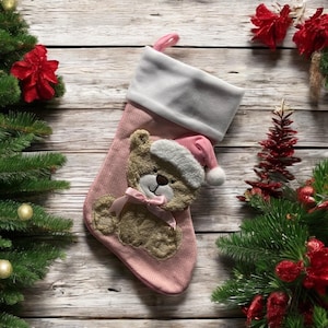 May include: Pink Christmas stocking with a white cuff and a brown teddy bear applique wearing a Santa hat.