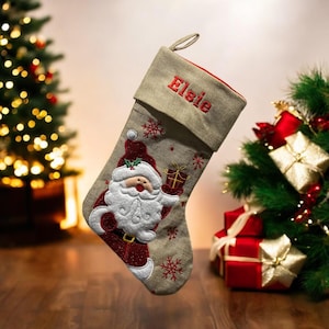 May include: A beige Christmas stocking with a red and white Santa Claus design. The stocking is personalised with the name "Elsie" in red embroidery.