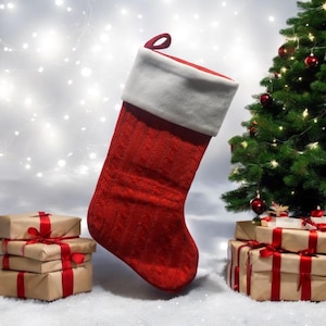 Op de afbeelding: Een rode en witte kerstsok met een witte boord en een gebreid patroon. De sok hangt tegen een witte achtergrond met een kerstboom op de achtergrond.