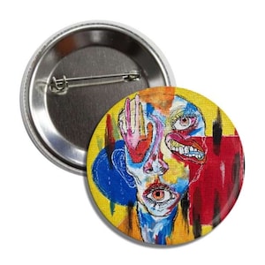 May include: A colorful button featuring a surreal portrait of a face with a hand covering one eye, a large eye, and a mouth with teeth. The background is a mix of yellow, blue, red, and black.