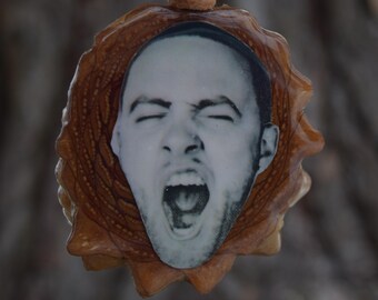 May include: A pendant featuring a black and white image of a person with their mouth open in a yell. The image is set in a brown, textured, circular frame, and hangs from a brown cord.