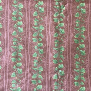 May include: A brown fabric with a repeating pattern of green vines. The vines have small green leaves and are arranged in vertical rows.