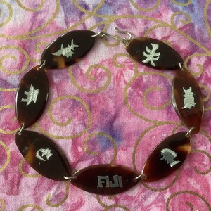 May include: A brown tortoiseshell necklace with silver accents. Each link features a different design, including a pagoda, a bird, a flower, and the word "Fiji".
