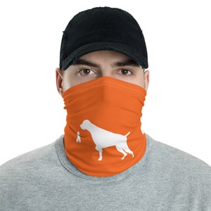 Puede incluir: Una persona con una gorra de béisbol negra y una máscara facial naranja con una silueta blanca de un perro que lleva un pájaro en la boca.