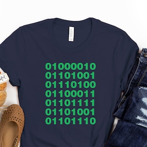 Op de afbeelding: Een donkerblauw t-shirt met een groene afbeelding van binaire code. De code luidt: 01000010 01101001 01110100 01100011 01101111 01110100 01101110.