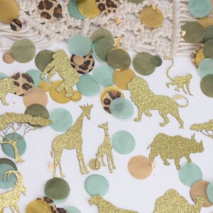 May include: Safari-themed confetti featuring gold glitter animal cutouts, such as lions and giraffes, mixed with green, tan, and leopard print circles. A macrame detail is visible in the background.