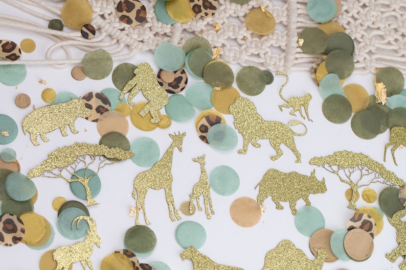 May include: Safari-themed confetti featuring gold glitter animal cutouts, such as lions and giraffes, mixed with green, tan, and leopard print circles. A macrame detail is visible in the background.