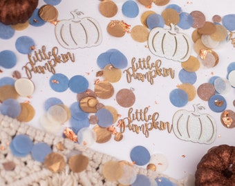 Op de afbeelding: Een feestelijke opstelling met goud, blauw en crème confetti, glitterende pompoen uitsparingen en de tekst "little pumpkin". Twee decoratieve pompoenen zijn ook aanwezig, wat een feestelijk thema creëert.