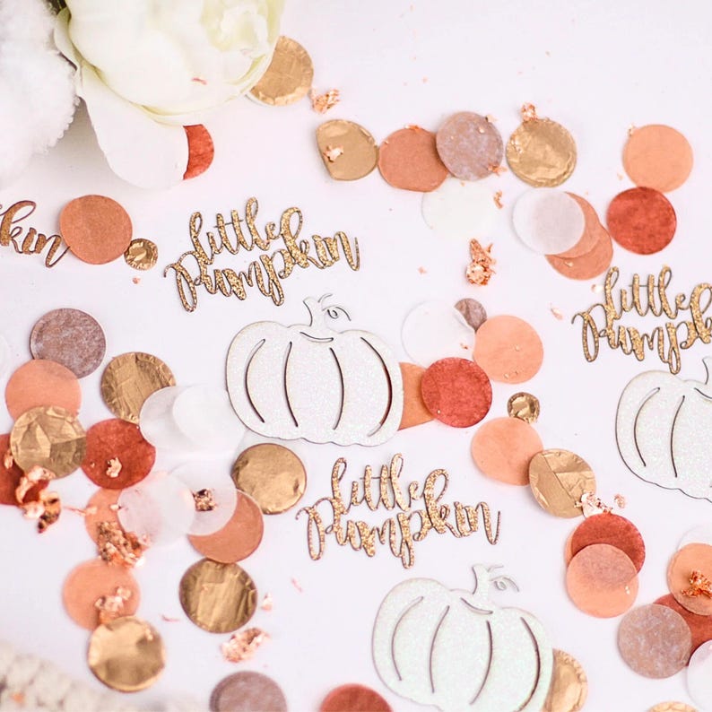 May include: White glitter pumpkin cutouts with the text "little pumpkin" in gold glitter. The cutouts are scattered on a white surface with peach, brown, and gold confetti.