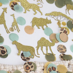 May include: Gold glitter animal cutouts including giraffes, lions, and elephants, scattered with confetti in shades of green, tan, and leopard print. The confetti is in various shapes and sizes, creating a playful safari theme.