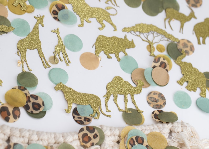 May include: Gold glitter animal cutouts including giraffes, lions, and elephants, scattered with confetti in shades of green, tan, and leopard print. The confetti is in various shapes and sizes, creating a playful safari theme.