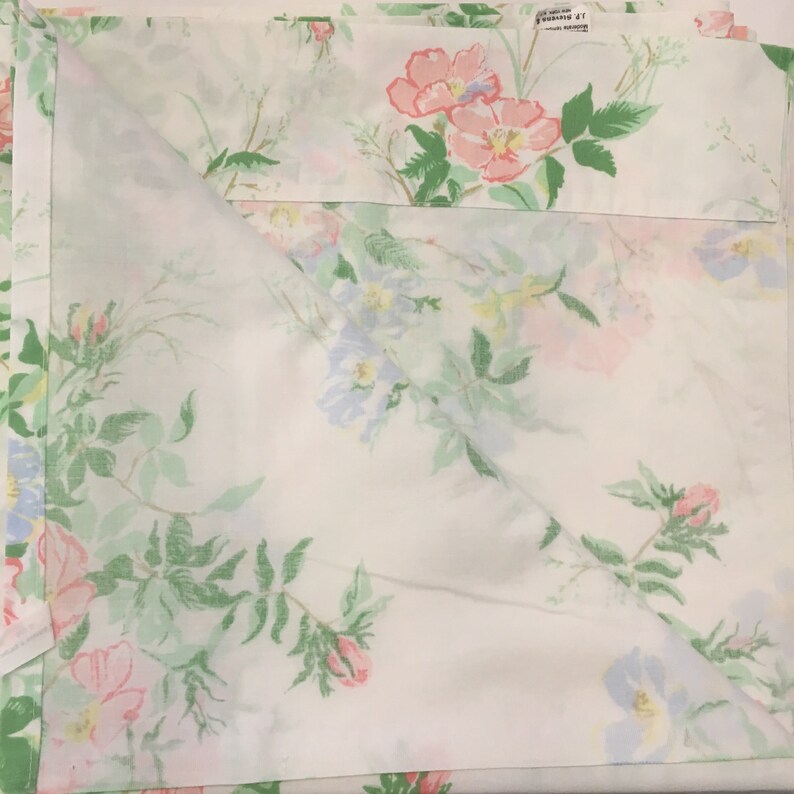 Puede incluir: Juego de s&aacute;banas blancas con estampado floral de flores rosas, azules y amarillas y hojas verdes. Las flores est&aacute;n en plena floraci&oacute;n y las hojas son de un verde vibrante. Las s&aacute;banas est&aacute;n dobladas, mostrando el patr&oacute;n.