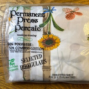 May include: A twin fitted sheet in a plastic package. The sheet features a floral pattern with sunflowers, butterflies, and bamboo stalks. The packaging reads "Permanent Press Percale" and "Twin Fitted Sheet for 39 x 75 in. Mattress."