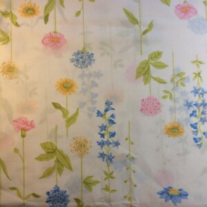 May include: White fabric with a floral pattern featuring pink, yellow, and blue flowers with green stems and leaves. The flowers are in various shapes and sizes, creating a delicate, repeating design.