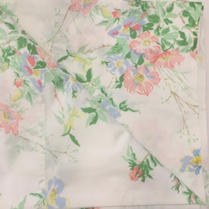 Puede incluir: S&aacute;bana blanca con un estampado floral. El dise&ntilde;o presenta flores rosas, azules y amarillas con hojas verdes. Las flores est&aacute;n esparcidas por la s&aacute;bana, creando un dise&ntilde;o delicado y femenino.