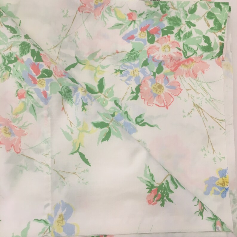 Puede incluir: S&aacute;bana blanca con un estampado floral. El dise&ntilde;o presenta flores rosas, azules y amarillas con hojas verdes. Las flores est&aacute;n esparcidas por la s&aacute;bana, creando un dise&ntilde;o delicado y femenino.