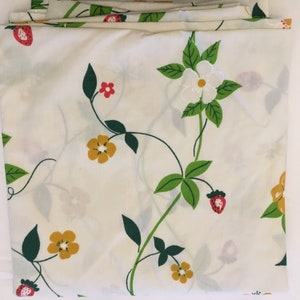 May include: Folded white fabric with a repeating pattern of strawberries, yellow flowers, and green leaves on winding vines. The design includes small red flowers and white blossoms. The fabric is folded neatly.