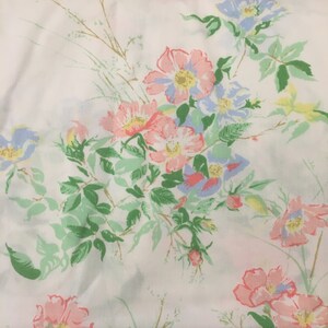 Puede incluir: Tela blanca con un estampado floral. El patr&oacute;n incluye flores rosas, azules y amarillas, complementadas con hojas y tallos verdes. Las flores tienen un aspecto vintage, pintado a mano.
