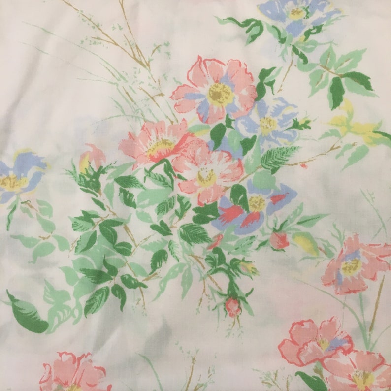 Puede incluir: Tela blanca con un estampado floral. El patr&oacute;n incluye flores rosas, azules y amarillas, complementadas con hojas y tallos verdes. Las flores tienen un aspecto vintage, pintado a mano.