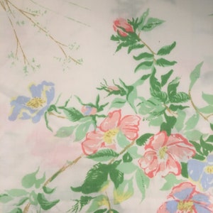 Puede incluir: Primer plano de una tela blanca con un estampado floral. El dise&ntilde;o presenta flores rosas, azules y amarillas con hojas y tallos verdes. Las flores est&aacute;n dispersas por la tela, creando una est&eacute;tica vintage.