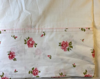 May include: White bed sheet with a floral pattern. The pattern features pink roses and green leaves on a white background. A thin pink stripe borders the floral section.