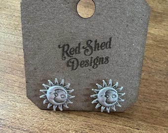 May include: Silver-toned sun and moon stud earrings on a brown cardboard display card. The earrings feature a sunburst design with a crescent moon face in the center. The card has a circular hole and the text "Red Shed Designs".