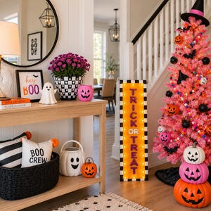 Puede incluir: Un &aacute;rbol de Navidad artificial rosa decorado con murci&eacute;lagos negros, pompones coloridos y peque&ntilde;as calabazas, rematado con un sombrero de bruja negro. Al lado hay un letrero luminoso rectangular con borde blanco y negro que dice TRICK OR TREAT.