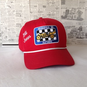 May include: A red baseball cap with a white rope brim. The cap features a patch with the text "Indianapolis 500 OLDTIMERS" and an image of a yellow race car. The name "Bill Jones" is embroidered on the side.